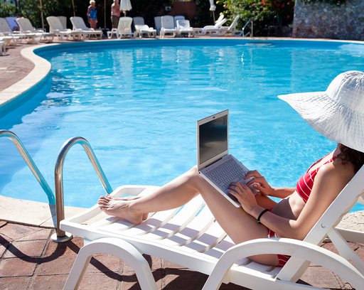 Young woman in big hat relaxing near the pool with laptop
